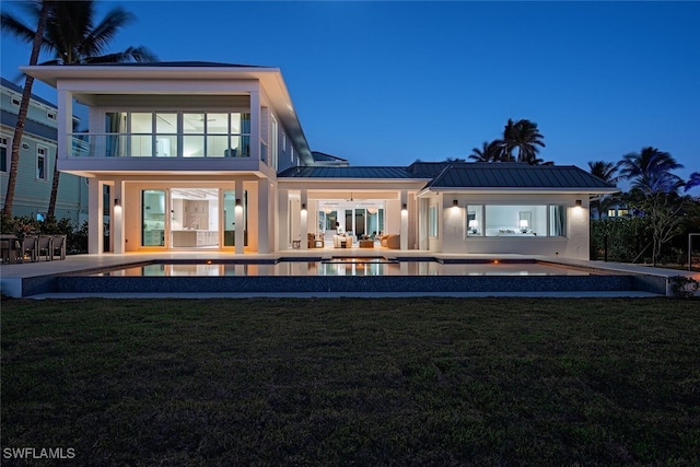 back house at dusk with a yard, a patio, and a balcony