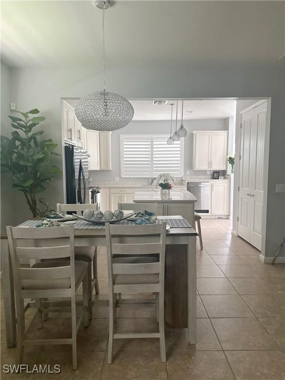 kitchen with hanging light fixtures, fridge, light tile patterned floors, and white cabinetry