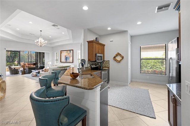 kitchen featuring a kitchen bar, appliances with stainless steel finishes, decorative light fixtures, dark stone countertops, and sink