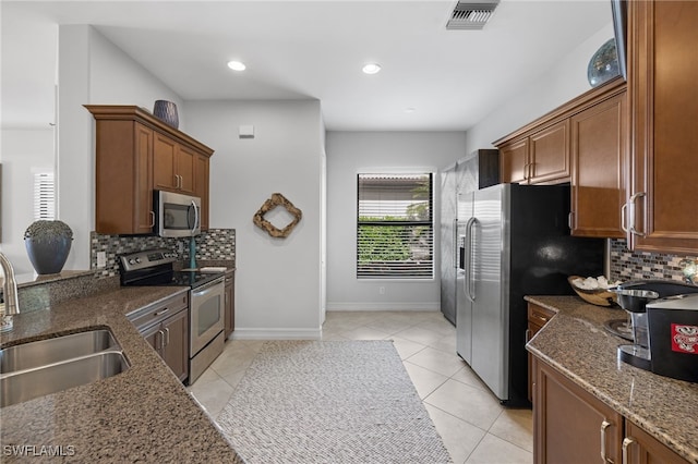 kitchen with appliances with stainless steel finishes, sink, dark stone countertops, and light tile patterned flooring