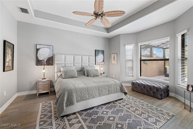 bedroom featuring ceiling fan, multiple windows, a tray ceiling, and hardwood / wood-style floors