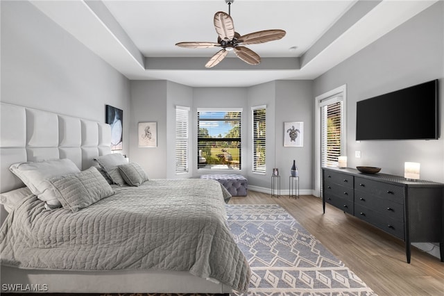 bedroom with ceiling fan, light hardwood / wood-style floors, and a tray ceiling