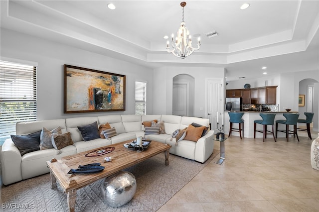 living room featuring light tile patterned flooring, a tray ceiling, and an inviting chandelier