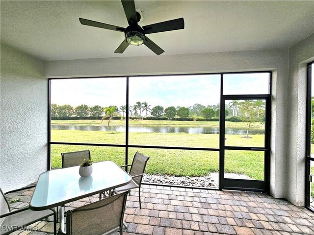 sunroom featuring ceiling fan and a water view