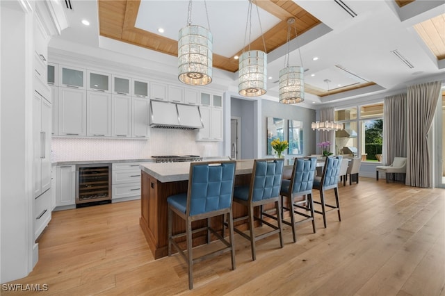 kitchen with wine cooler, tasteful backsplash, light wood-style floors, a large island with sink, and extractor fan