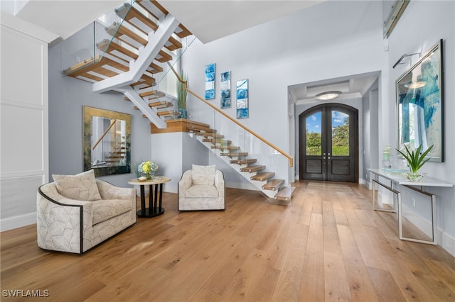 entryway featuring arched walkways, french doors, wood-type flooring, stairway, and a high ceiling