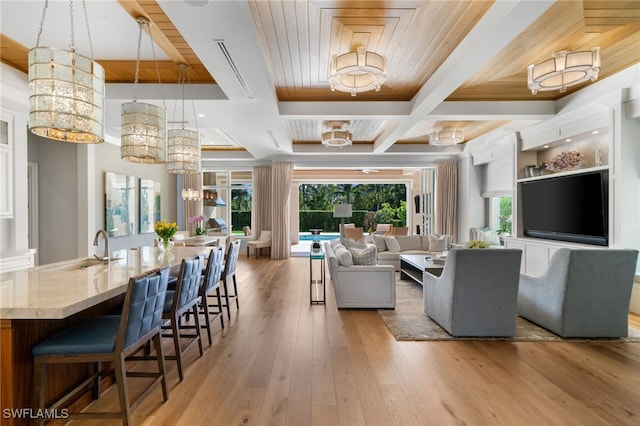 living area featuring light wood finished floors, coffered ceiling, ornamental molding, a notable chandelier, and beam ceiling