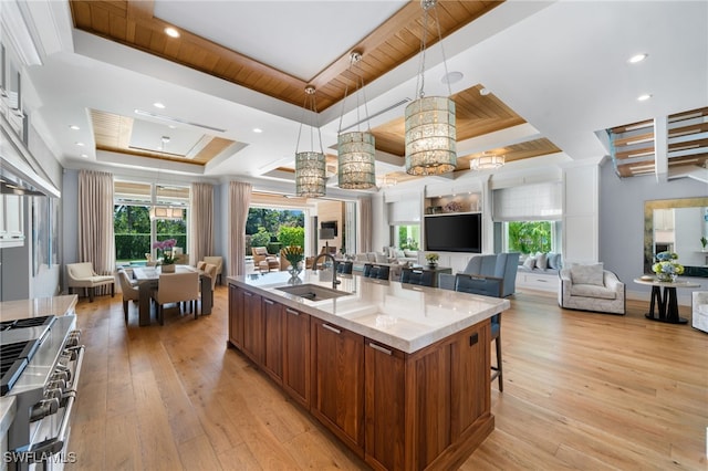 kitchen with a tray ceiling, light wood finished floors, open floor plan, a sink, and double oven range