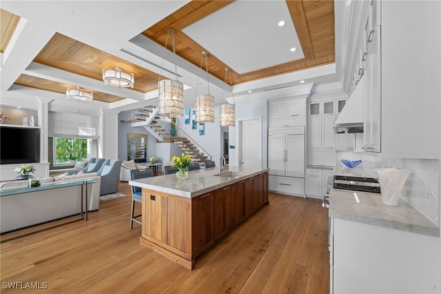 kitchen featuring light wood finished floors, a raised ceiling, white cabinetry, a sink, and a kitchen bar