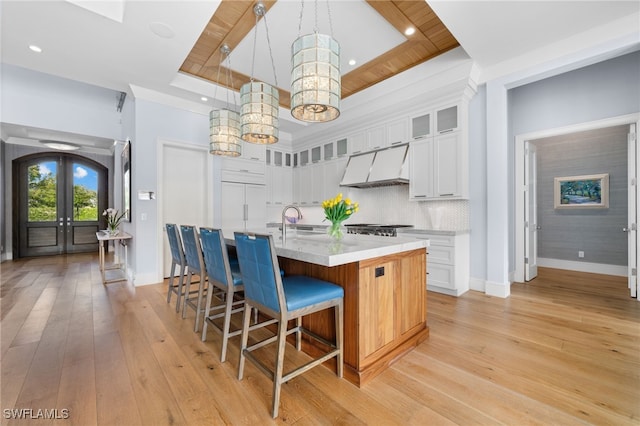 kitchen featuring a tray ceiling, french doors, light countertops, custom range hood, and a sink