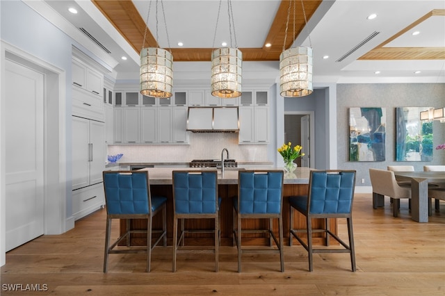 kitchen featuring an island with sink, light wood finished floors, white cabinets, and decorative backsplash