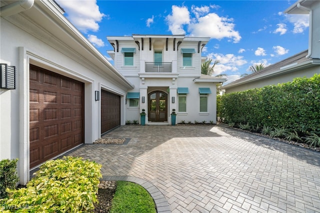 view of front of home featuring decorative driveway, french doors, a balcony, and stucco siding