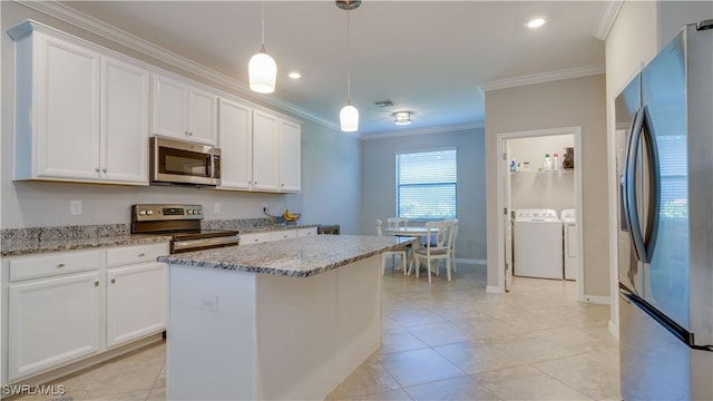 kitchen with a kitchen island, washing machine and dryer, white cabinetry, hanging light fixtures, and stainless steel appliances