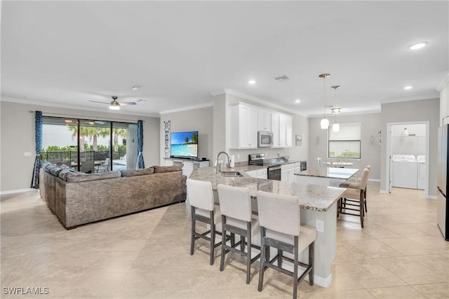17250 Ashcomb Way, Estero, FL 33928 - kitchen featuring appliances with stainless steel finishes, washing machine and dryer, ornamental molding, a sink, and white cabinetry