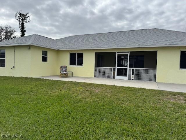 back of property with stucco siding, a shingled roof, a patio, and a yard