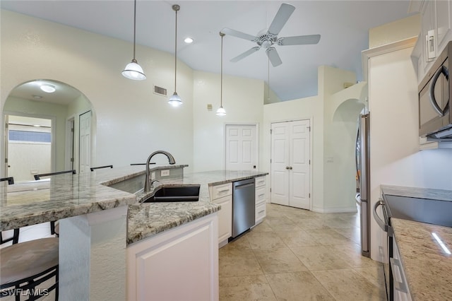 kitchen featuring a kitchen bar, appliances with stainless steel finishes, decorative light fixtures, light stone countertops, and sink