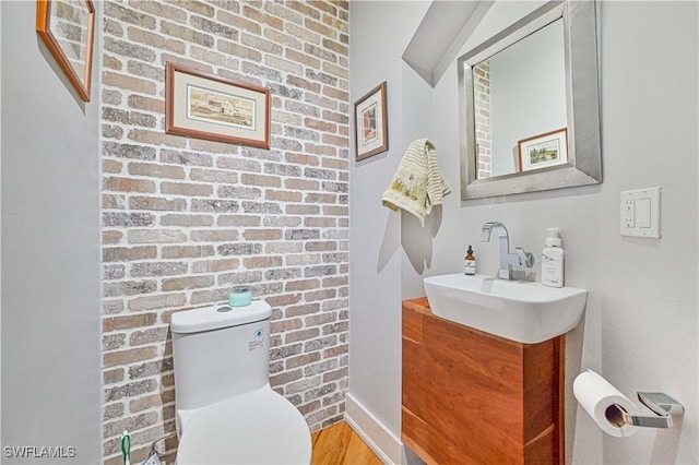 bathroom with brick wall, hardwood / wood-style floors, toilet, and vanity