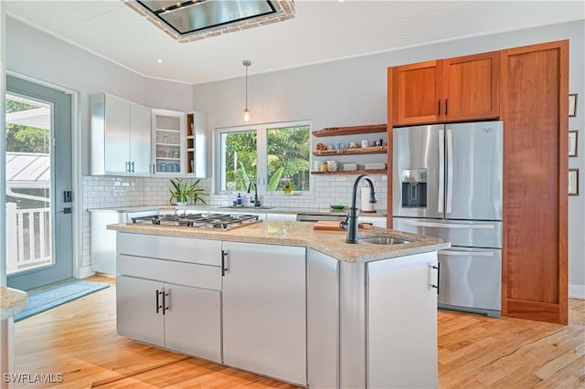 kitchen featuring decorative light fixtures, white cabinetry, an island with sink, range hood, and stainless steel appliances