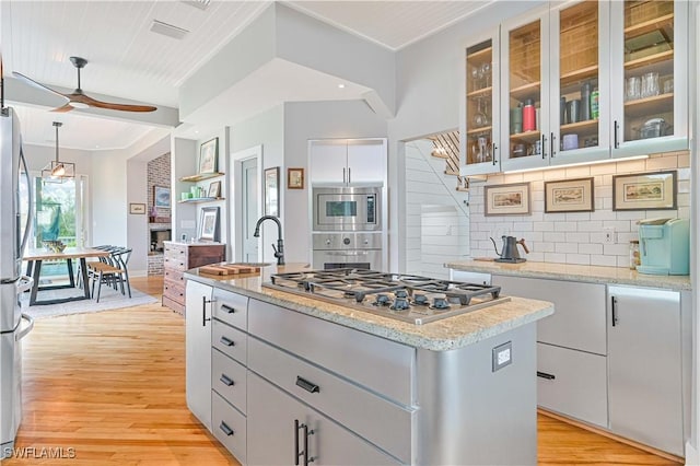 kitchen featuring appliances with stainless steel finishes, light hardwood / wood-style floors, backsplash, ceiling fan, and a center island with sink