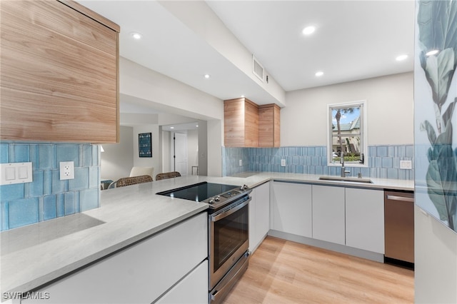 kitchen featuring backsplash, light hardwood / wood-style floors, sink, white cabinetry, and appliances with stainless steel finishes