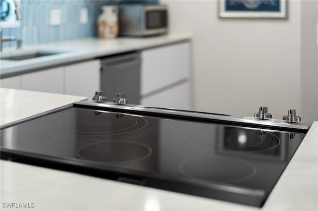 interior details with white cabinets, dishwashing machine, cooktop, and sink