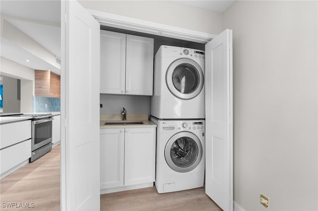 laundry room featuring cabinets, sink, stacked washer and clothes dryer, and light wood-type flooring