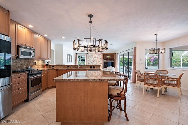 kitchen with pendant lighting, appliances with stainless steel finishes, a kitchen bar, kitchen peninsula, and a notable chandelier