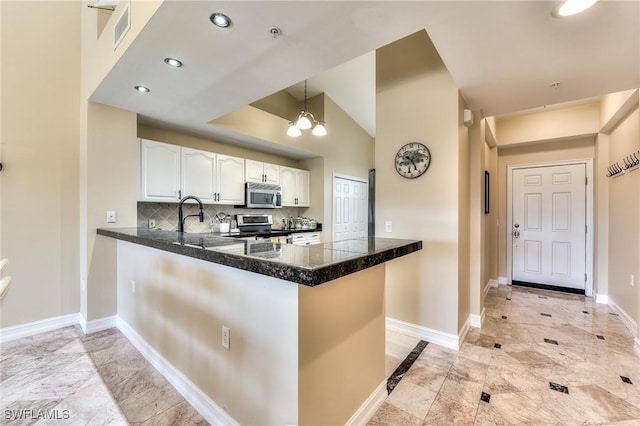 kitchen with kitchen peninsula, appliances with stainless steel finishes, decorative backsplash, white cabinets, and a chandelier