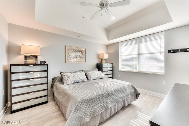 bedroom with light wood-type flooring, a raised ceiling, and ceiling fan