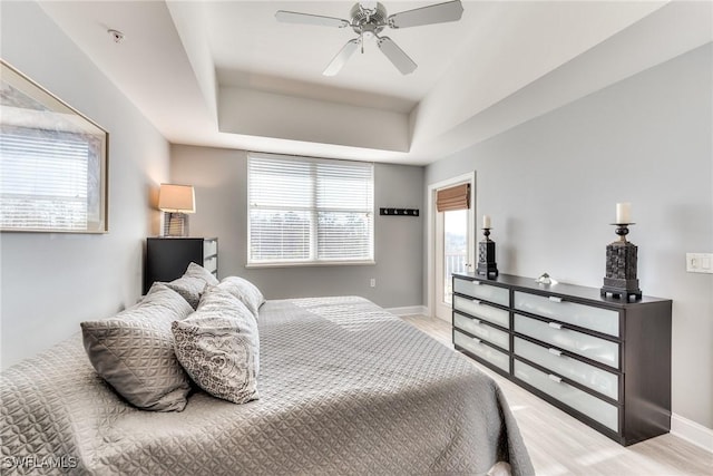 bedroom with a raised ceiling, multiple windows, ceiling fan, and light wood-type flooring