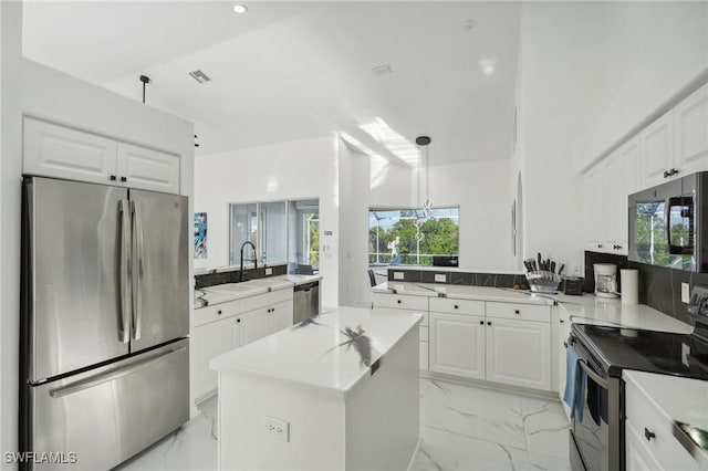 kitchen featuring appliances with stainless steel finishes, a kitchen island, sink, decorative light fixtures, and white cabinetry