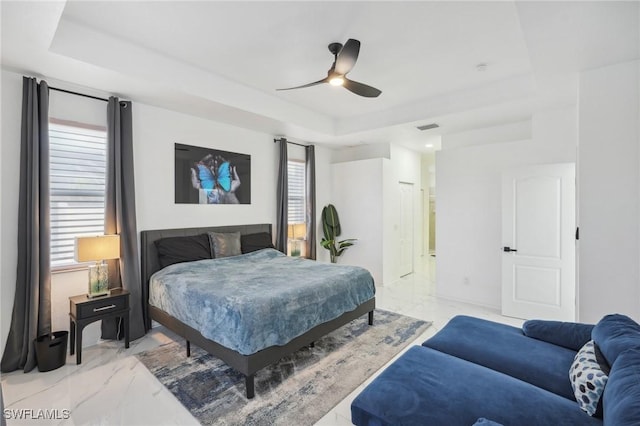 bedroom with ceiling fan, multiple windows, and a tray ceiling