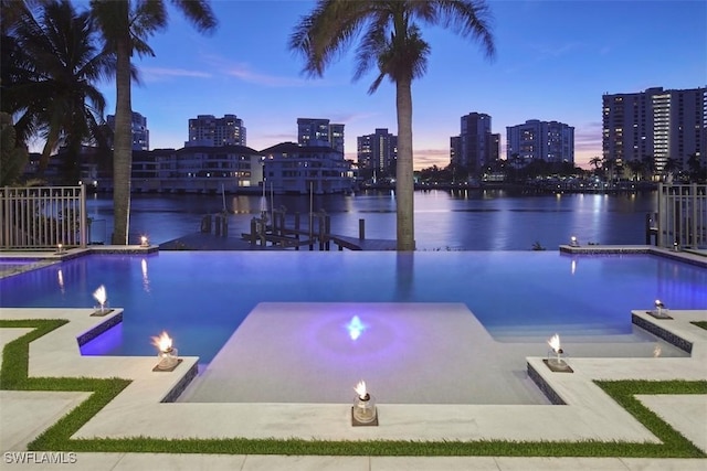 pool at dusk with a water view, an outdoor fire pit, and a hot tub