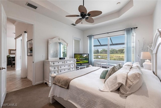 tiled bedroom with ceiling fan and a tray ceiling