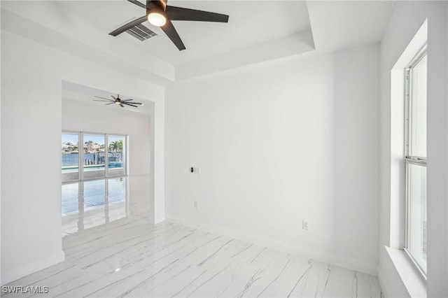 empty room with a raised ceiling, ceiling fan, and a healthy amount of sunlight