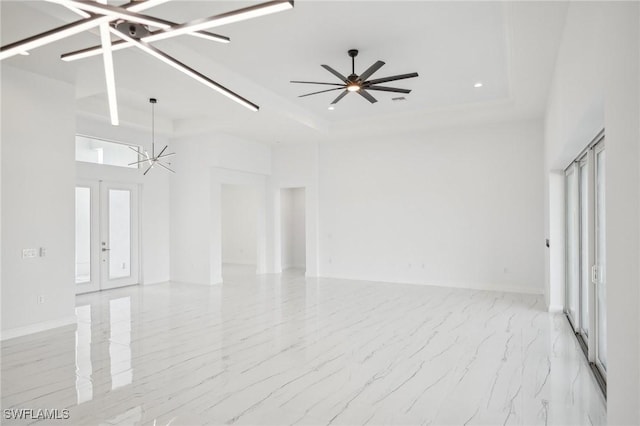 spare room with ceiling fan with notable chandelier, a raised ceiling, and french doors