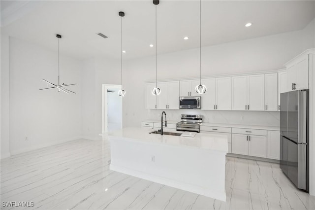 kitchen featuring pendant lighting, white cabinets, stainless steel appliances, and a center island with sink