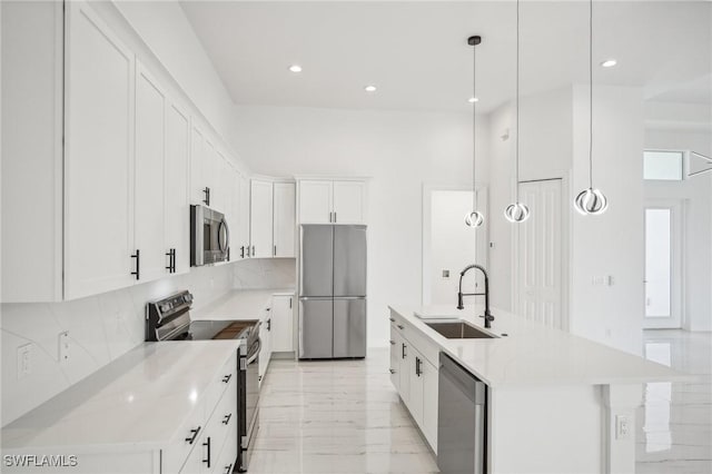 kitchen with white cabinetry, sink, hanging light fixtures, stainless steel appliances, and a kitchen island with sink