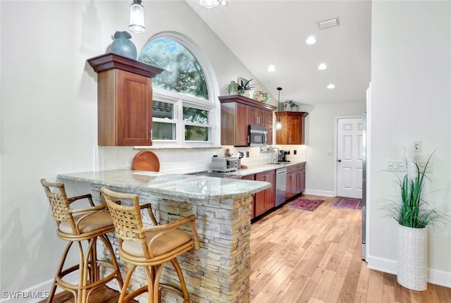 kitchen with kitchen peninsula, tasteful backsplash, stainless steel appliances, vaulted ceiling, and decorative light fixtures