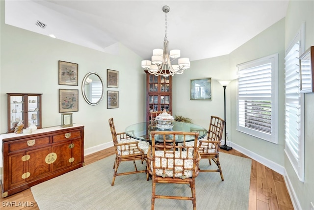 dining area with a chandelier, light wood-type flooring, and vaulted ceiling