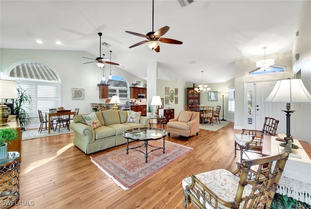 living room featuring ceiling fan with notable chandelier, vaulted ceiling, and light wood-type flooring