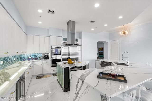 kitchen featuring appliances with stainless steel finishes, white cabinets, light stone counters, a kitchen island, and decorative backsplash