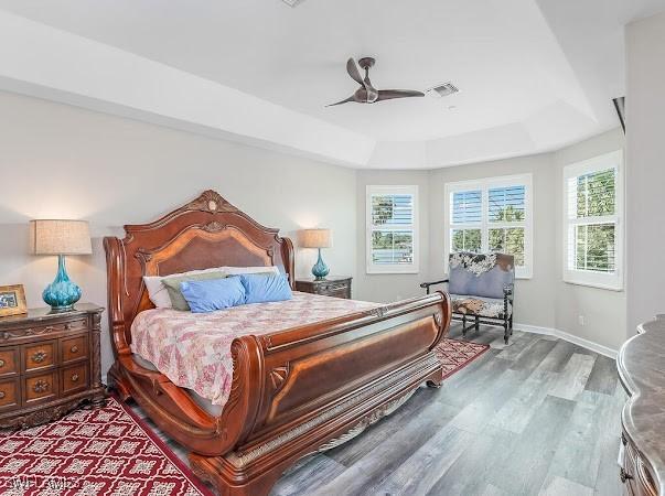 bedroom featuring ceiling fan, multiple windows, hardwood / wood-style flooring, and a raised ceiling