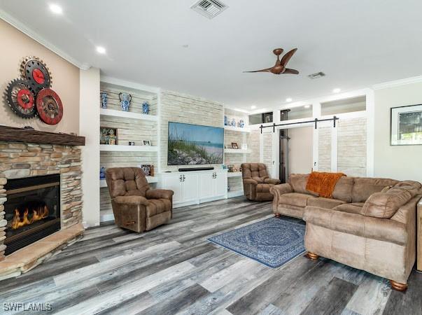 living room with wood-type flooring, a fireplace, built in features, ceiling fan, and crown molding