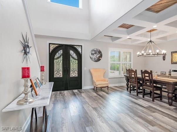 foyer entrance with an inviting chandelier, coffered ceiling, wood-type flooring, french doors, and beam ceiling