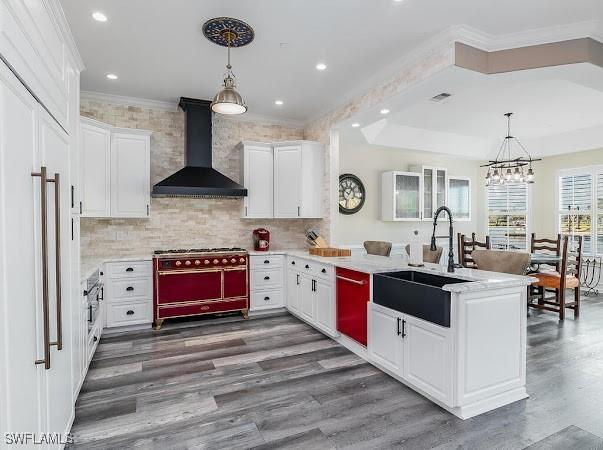 kitchen with decorative light fixtures, wall chimney range hood, sink, range with two ovens, and white cabinets