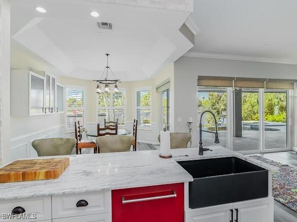 kitchen with a chandelier, light stone countertops, sink, and white cabinetry