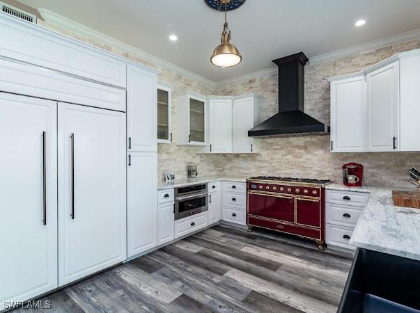 kitchen featuring wall chimney range hood, double oven range, white cabinetry, stainless steel oven, and ornamental molding