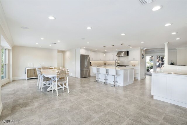 kitchen with wall chimney exhaust hood, light countertops, high end refrigerator, and white cabinets