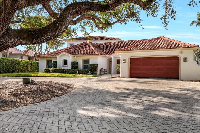 mediterranean / spanish home with a garage, decorative driveway, a tiled roof, and stucco siding